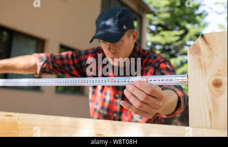 Man uses a tape measure to mark the length of a piece of lumber. Stock Photo