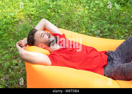A young man lies on an air mattress or sofa with his eyes closed, smiles, dreams and rests. Pleasant pastime, relaxation in nature Stock Photo