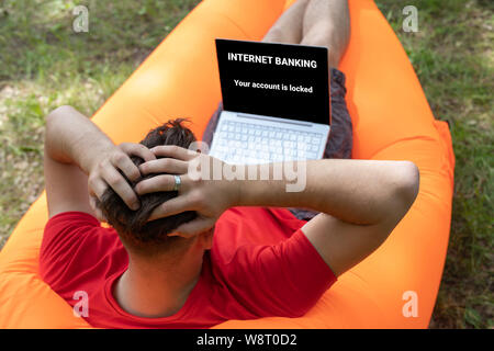Online scam concept, internet banking error. Your accaunt is locked on laptop screen.  alarmed man clutching his head Stock Photo