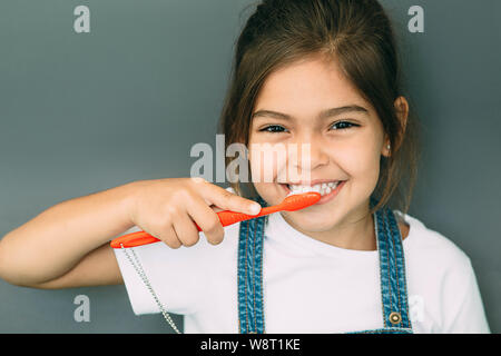 Yes, my teeth is clean. Cute mixed raced girl brushing teeth at gray background. Stock Photo