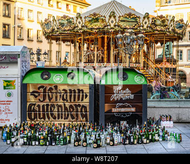 Empty glass bottles dumped in front of overflowing bottle banks, merry-go-round in background, Strasbourg, Alsace, France, Europe, Stock Photo