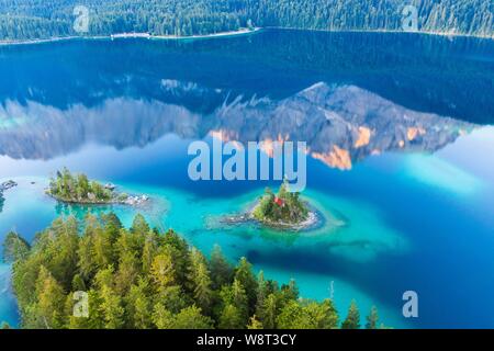 Eibsee lake with Braxen and Schonbichl islands, water reflection of the Zugspitze in the morning light, near Grainau, Werdenfelser Land, aerial Stock Photo