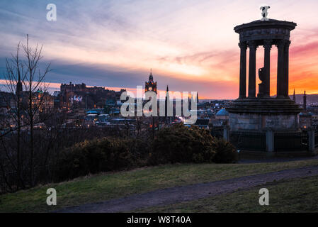 Edinburgh Skyline as seen from Calton Hill at Dusk. A monument and a gravel path are visible in foreground.