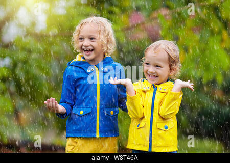 Kids play in autumn rain. Child playing outdoor on rainy day. Little boy catching rain drops under heavy shower. Fall storm in a park. Waterproof wear Stock Photo