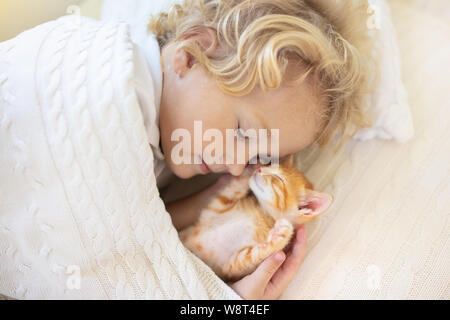 Baby boy sleeping with kitten on white knitted blanket. Child and cat. Kids and pets. Little kid with his animal. Cozy winter evening with pet. Childr Stock Photo