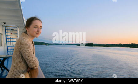 Woman admiring landscape from deck of cruise ship after sunset Stock Photo