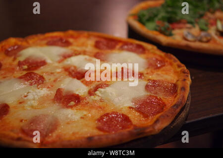 Salami pizza with buffalo cheese and seafood pizza with shrimp, squid, clam and lettuce topping on round wood tray Stock Photo