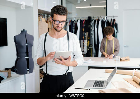 Young serious male tailor with tablet looking through online creative ideas Stock Photo