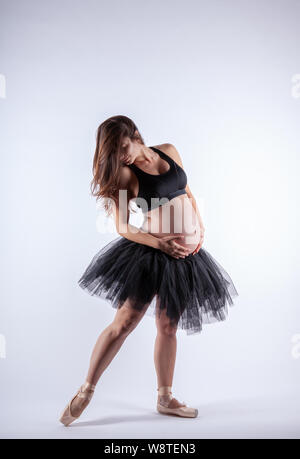 Young beautiful pregnant ballerina with black dress is posing in studio. Stock Photo