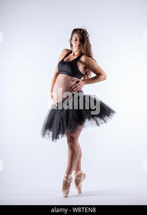 Young beautiful pregnant ballerina with black dress is posing in studio. Stock Photo