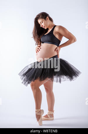 Young beautiful pregnant ballerina with black dress is posing in studio. Stock Photo