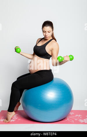Young pregnant woman doing gymnastics with fitball and dumbbells. Stock Photo
