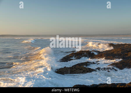waves crash over the rocks on a sunny evening at Westward Ho, Devon Stock Photo