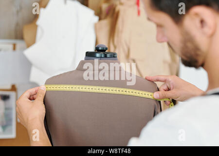 Male tailor measuring back of new jacket on dummy during work Stock Photo