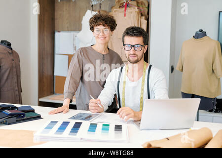 Young successful fashion designers using mobile gadgets while working in studio Stock Photo