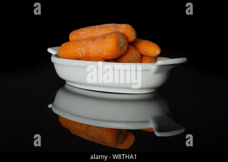 Lot of whole stale  orange stale baby carrot baby in a wooden bowl isolated on black glass Stock Photo