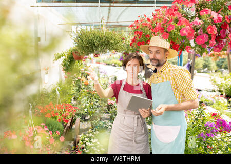 Two farmers of gardeners in aprons looking at one of flowers Stock Photo