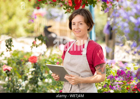 Happy female gardener with touchpad working over online price list Stock Photo