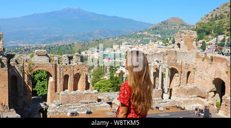 Beautiful young female model in the ruins of the ancient Greek theater in Taormina with the Etna volcano on the background, Sicily, Italy Stock Photo