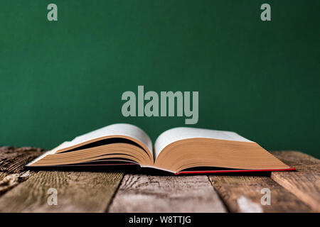 Back to school concept, open book on old wooden surface against a backdrop of clean green chalk board, selective focus, copyspace Stock Photo