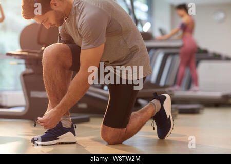 Side view portrait of muscular man tying shoelaces in gym, copy space Stock Photo
