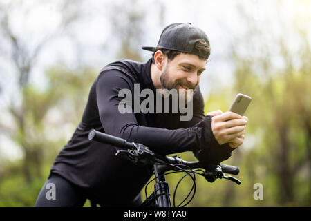 Happy bearded man cyclist rides in the sunny forest on a mountain bike. Stock Photo