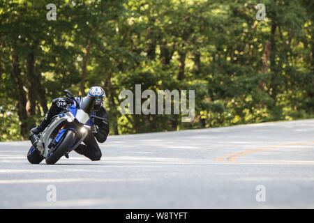 A man riding a road racing motorcycle leans into a turn at a high rate of speed, as he traverses windy roads on June 9, 2018 in Blairsville, GA. Stock Photo