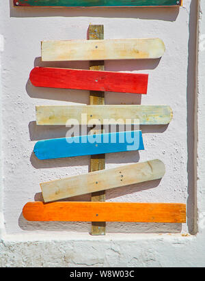 Colored blank wooden signboards pointing to different directions on a white wall.  Tall post with six wooden signs points to various destinations from Stock Photo