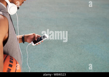 Closeup of unrecognizable African-American man holding basketball and using smartphone outdoors, copy space background Stock Photo