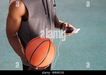 Mid section of unrecognizable African-American man holding basketball and using smartphone outdoors, copy space background Stock Photo