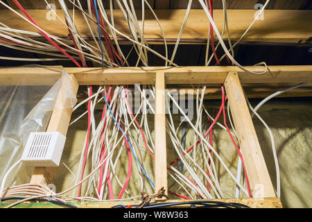 Exposed wiring in opened stud wall with yellow foam insulation in utility room in basement inside a residential home. Stock Photo