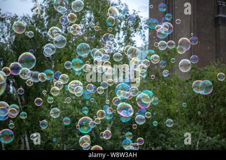 Many small soap bubbles created with sticks and rope seen floating in the grey London evening sky on a day in August. Stock Photo
