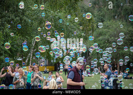 Tourists enjoying the many soap bubbles produced by a street entertainer with specialist tools on the South Bank in London. Stock Photo