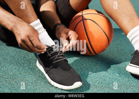 Closeup of African-American man tying sports shoes in basketball court outdoors, copy space background Stock Photo