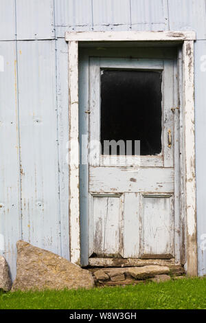 Old crooked grey wooden entrance door on corrugated sheet metal cladded building in residential backyard Stock Photo