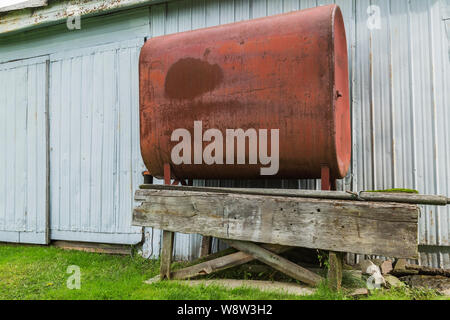 Red painted heating oil tank on old elevated wooden platform next to corrugated sheet metal cladded building in residential backyard Stock Photo