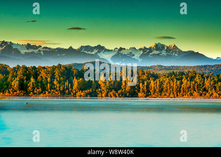 Dramatic light on the Peaks of the Southern Alps behind the forest and Okarito Lagoon Stock Photo