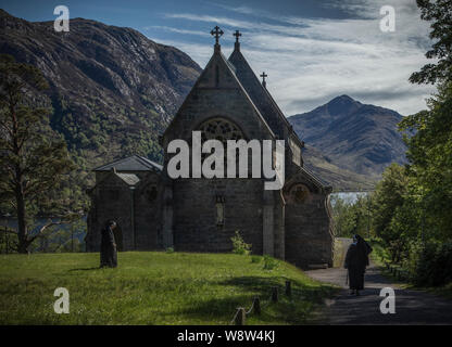 Church in Glenfinnan in the West Highlands of Scotland with two nuns approaching it and the wonderful mountains and Loch Shiel in the distance Stock Photo