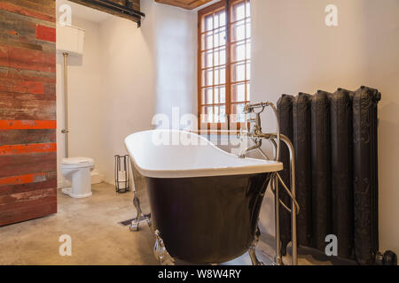 White and black freestanding chrome claw foot bathtub next to hot water heating radiator in bathroom inside old 1820 house Stock Photo