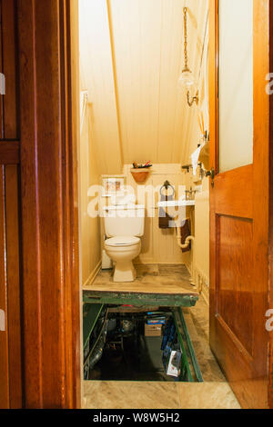 Water closet with white toilet and sink, plus opened trap door leading to basement laundry room inside an old 1927 American Four Squares house Stock Photo