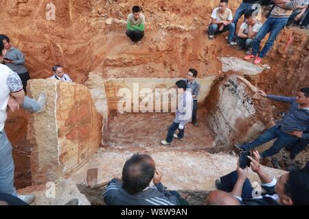 Chinese villagers gather to look at specialists from the Cultural Relics Bureau working in an ancient tomb where several Ming Dynasty paintings were d Stock Photo