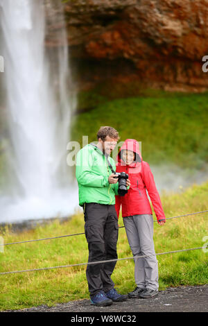 Tourists with SLR camera by waterfall on Iceland. Romantic couple visiting famous tourist attractions and landmarks in Icelandic nature landscape by Seljalandsfoss waterfall on Ring Road. Stock Photo