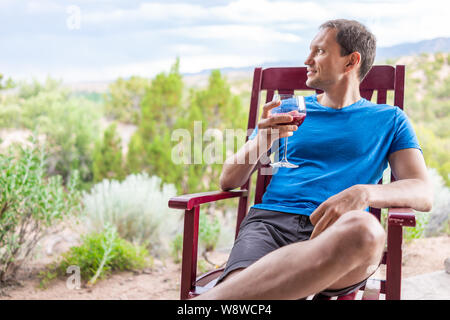 Man sitting outside in rocking chair drinking glass of red pink purple wine or cranberry juice in Santa Fe desert garden backyard Stock Photo
