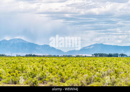 Highway South County Road 100 with countryside farms in Monte Vista, Colorado and view of Rocky Mountains Stock Photo