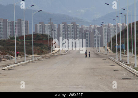 Two residents walk on an empty road near a cluster of empty newly-constructed residential apartment buildings in Chenggong district, Kunming city, sou Stock Photo