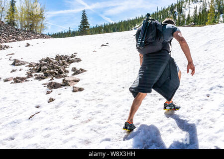 Man climbing uphill summit in Thomas Lakes Hike in Mt Sopris, Carbondale, Colorado in early 2019 summer with snow on peak Stock Photo
