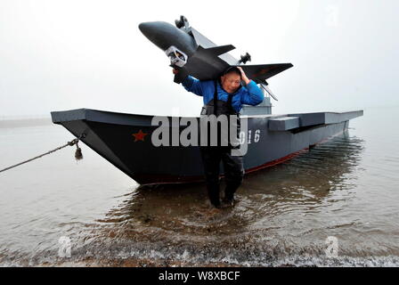 80-year-old Wen Yuzhu takes off a model of the J-20 stealth fighter from his homemade model of Chinas first aircraft carrier The Liaoning on a beach i Stock Photo
