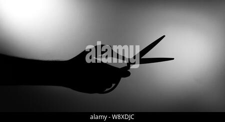 Man holds scissors in one hand silhouette Stock Photo