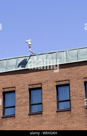 A security camera mounted on the rooftop of a brick building watches the city street below. Stock Photo