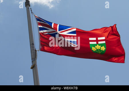 The flag of the Canadian province of Ontario flies on a flagpole against a blue sky. Stock Photo